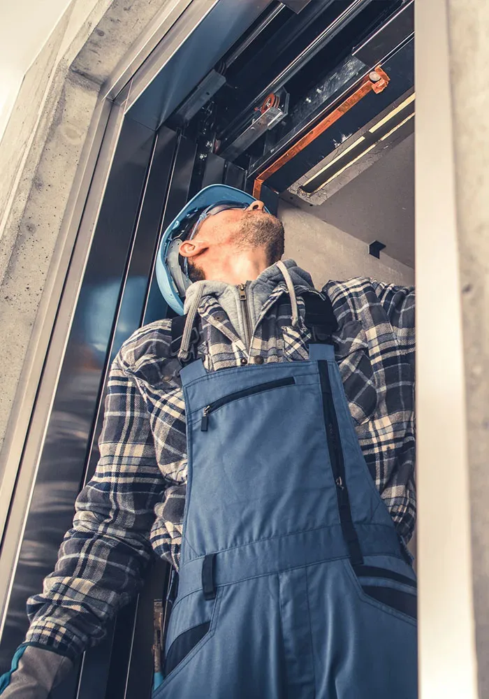 shutterstock_2246886695.jpg A man in overalls is working on an elevator.